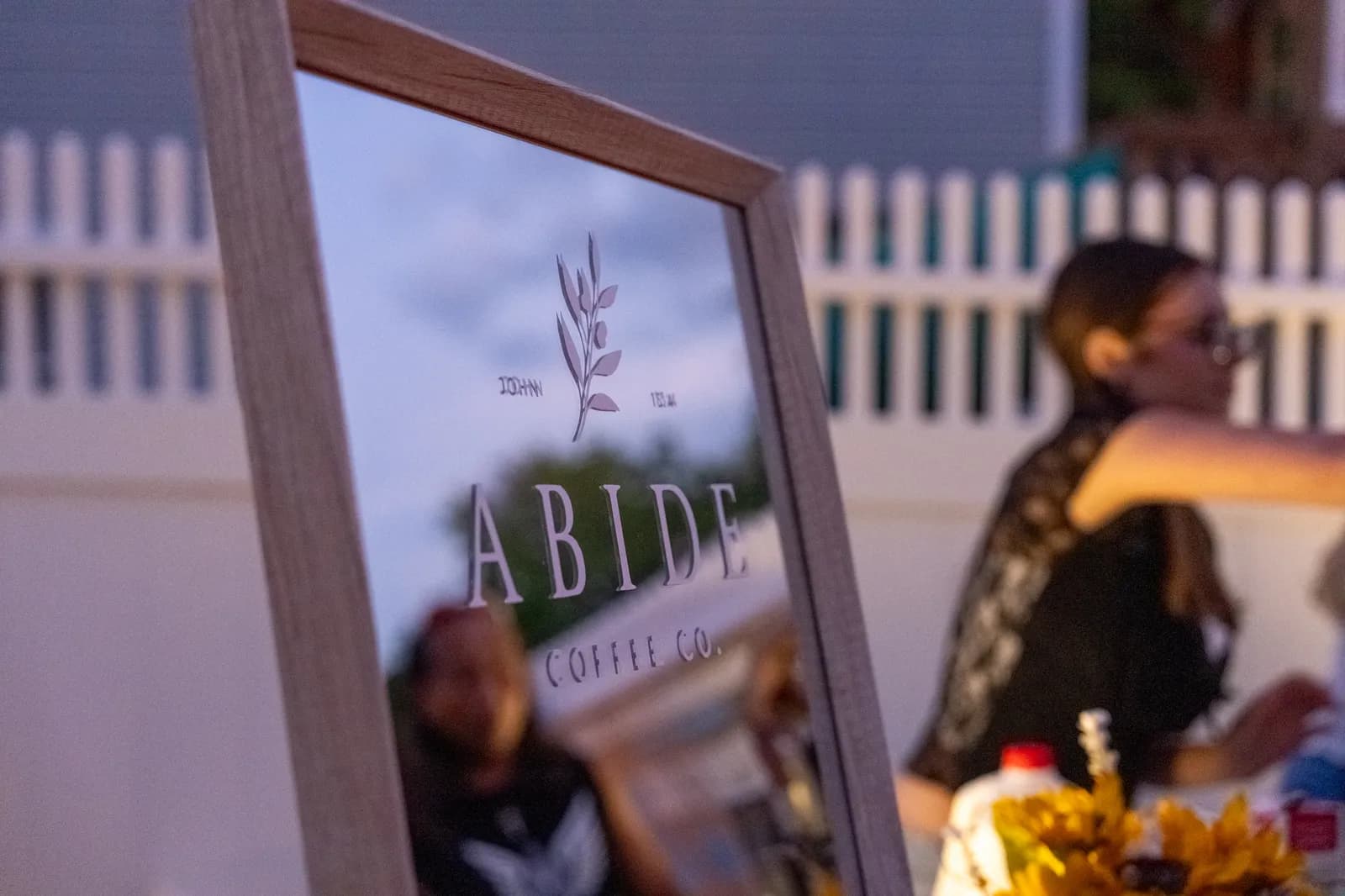 The A-frame Abide sign stands in the foreground as guests gather at dusk.