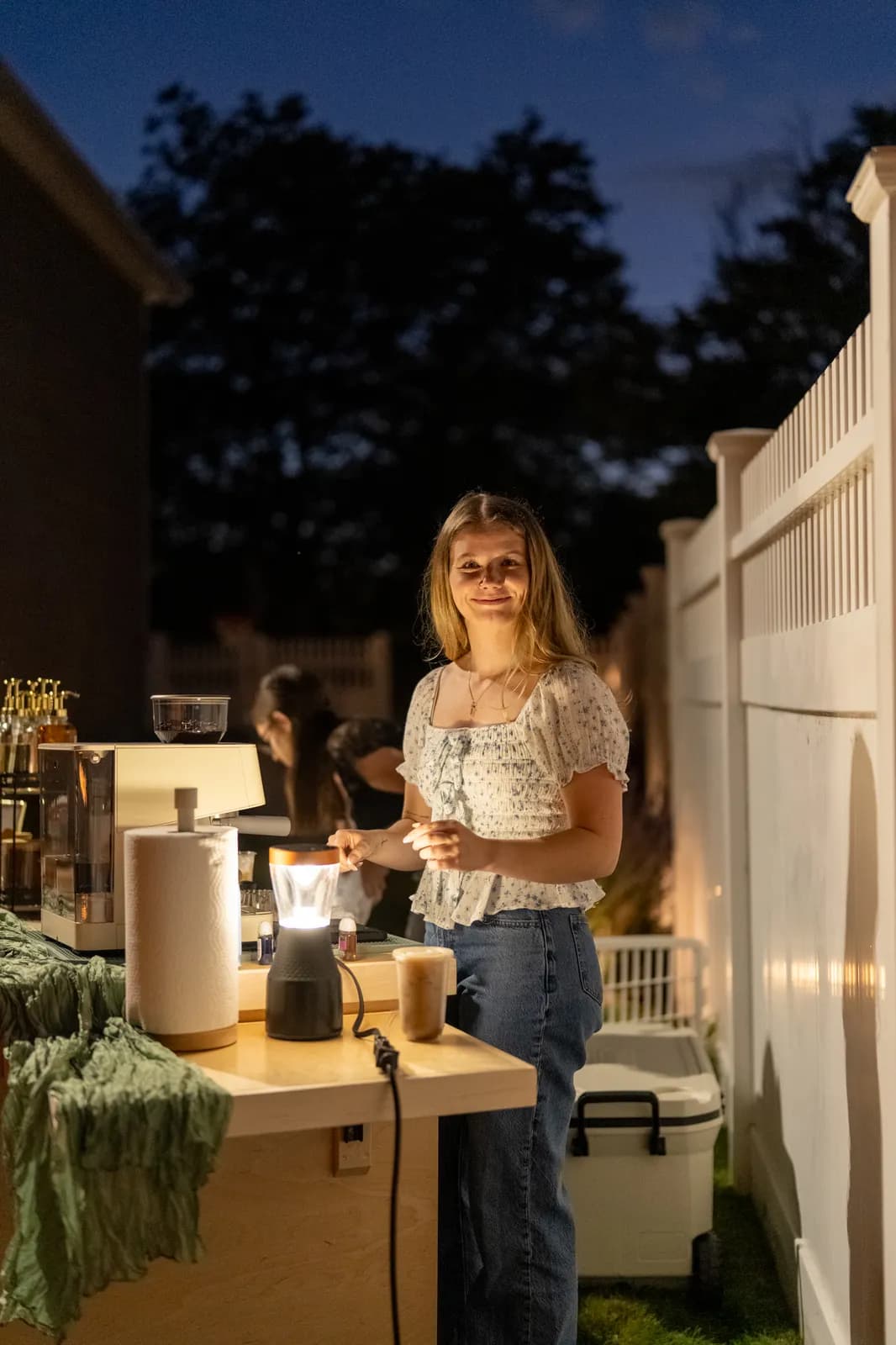 A barista works at the cart under warm lantern light after sundown.