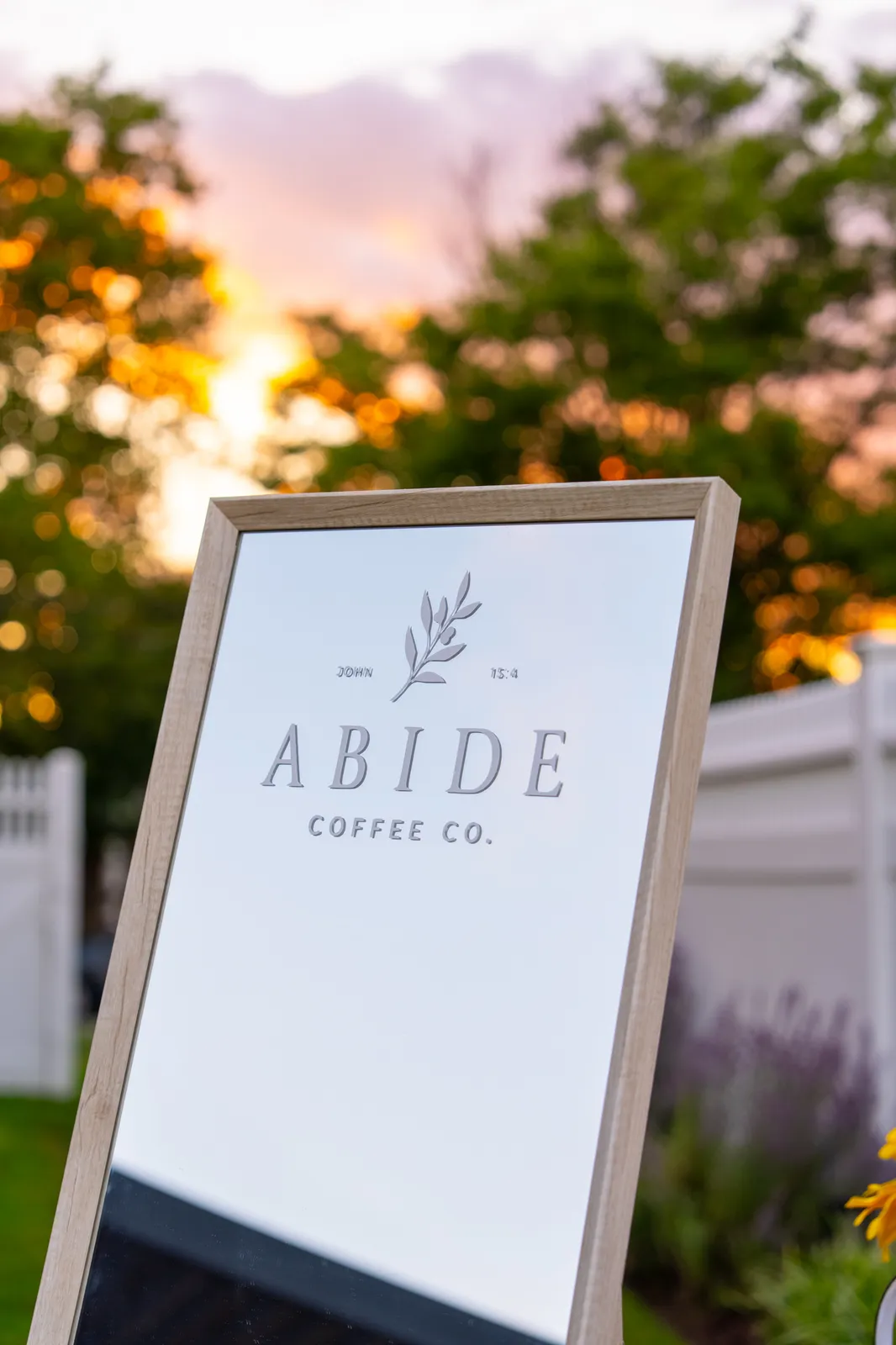 The wooden A-frame Abide Coffee Co. sign — “John 15:4” — catches the last of a warm sunset.